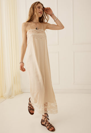 A woman models a long cream-colored slip dress with delicate lace trim at the bodice and hem