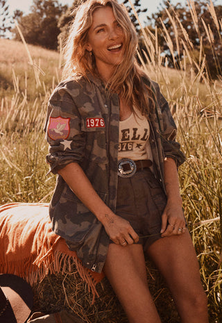  wearing a camouflage bomber jacket over a graphic tee and shorts.